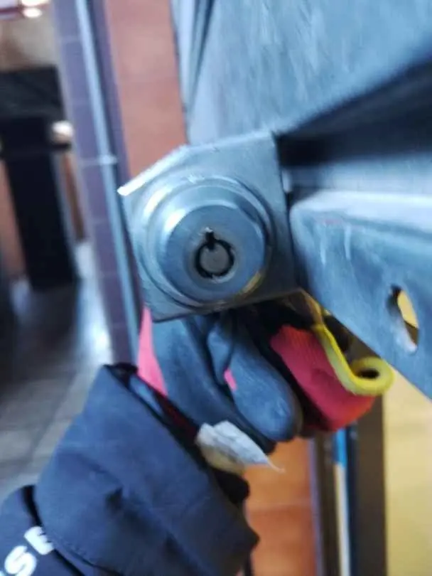Mano con guante sacando un bombín de una puerta con una herramienta