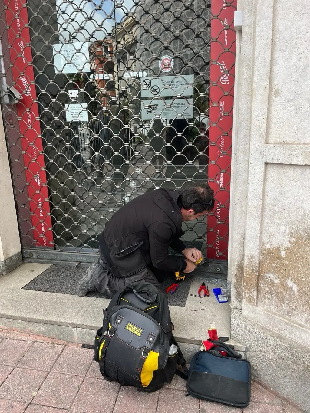 Iván de rodillas abriendo el cierre metálico de un local