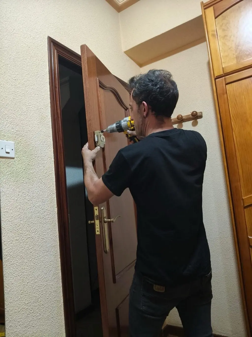 Iván taladrando la cerradura de una puerta de madera en un piso