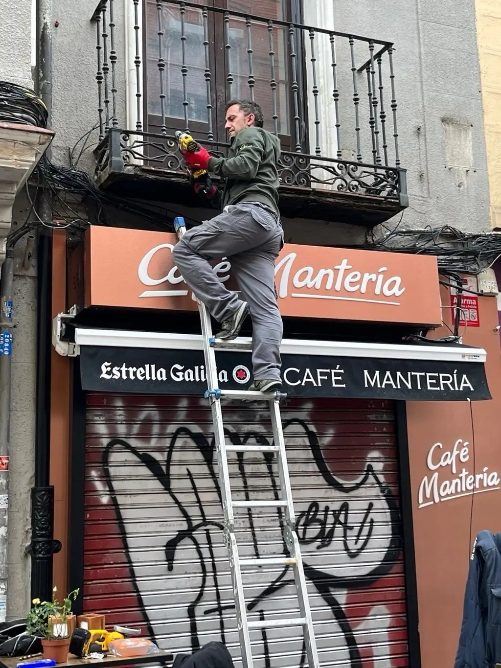Iván subido a una escalera trabajando en la fachada de un café
